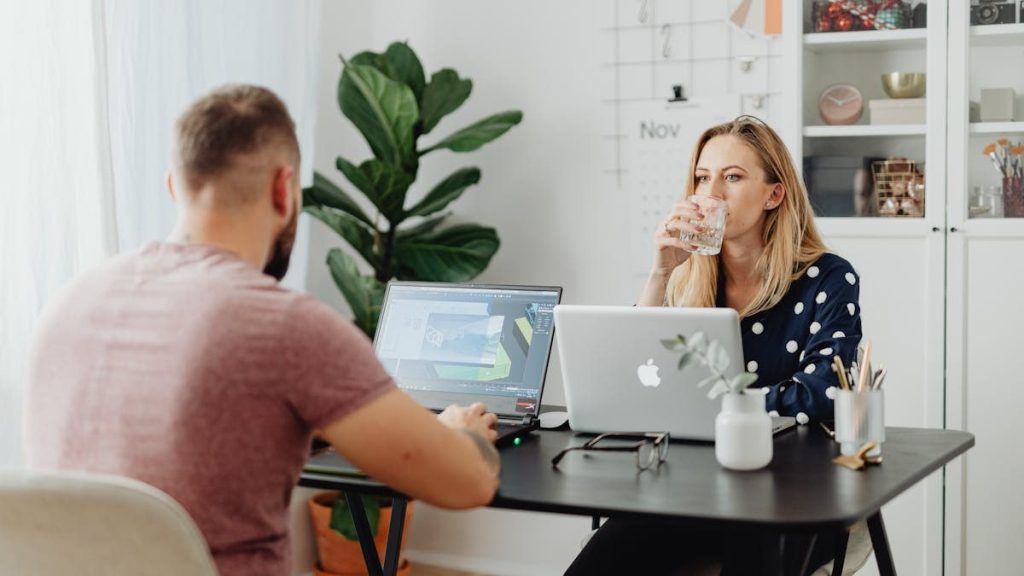 Two colleagues working in a stylish office space with laptops and beverages.